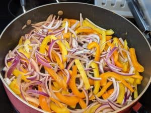 Slices of red onion and bell pepper in sauté pan