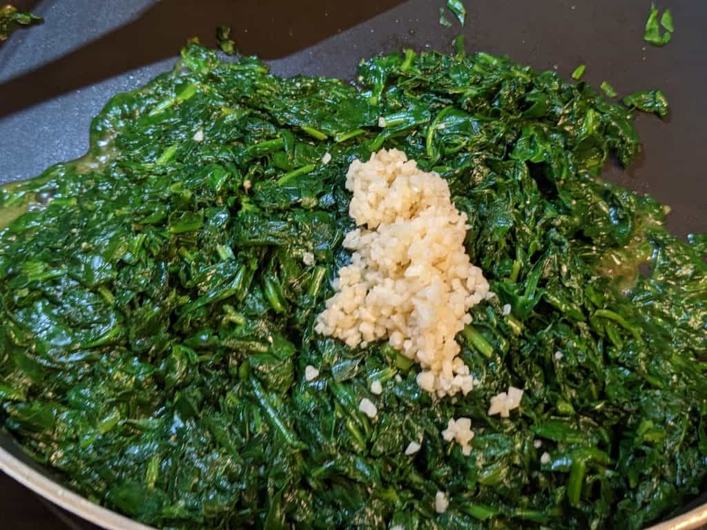 Cooked spinach in pan with garlic added but not yet combined