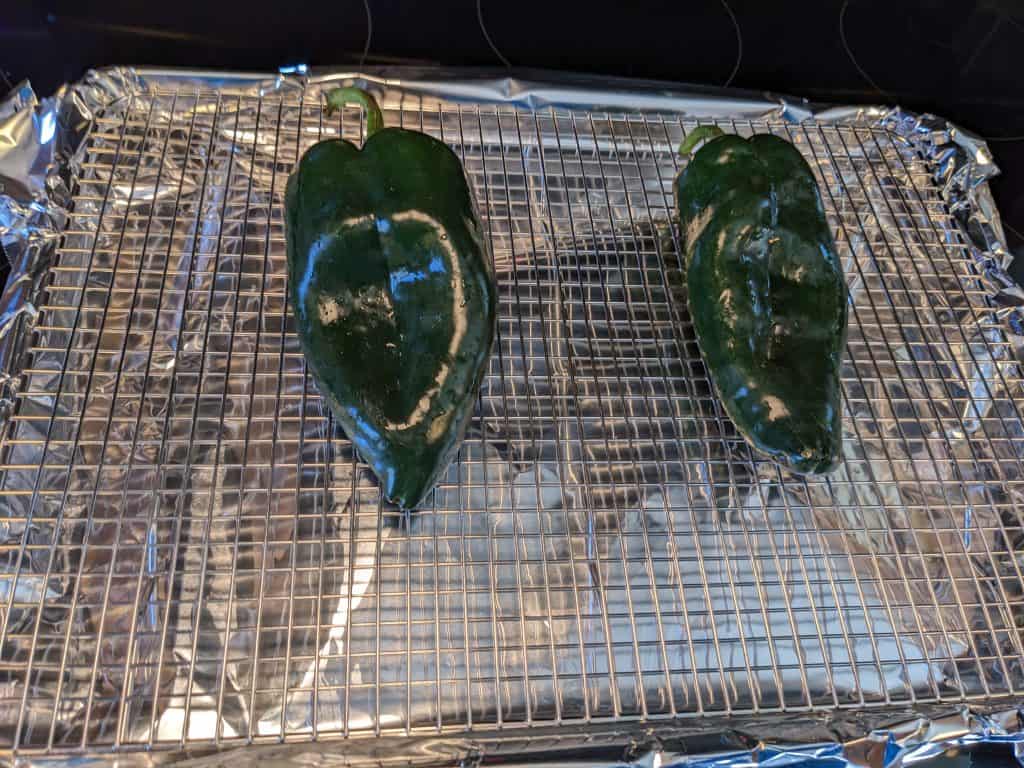 Two poblanos on wire rack insert on rimmed baking sheet
