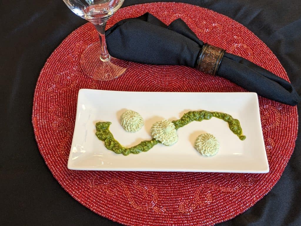 Place setting with whipped pesto and pesto styled on plate, black napkin in napkin ring, and empty wine glass