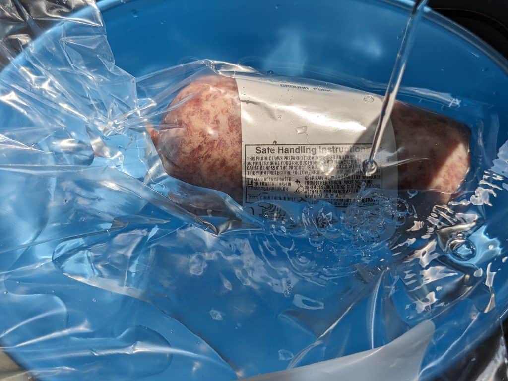 Meat thawing in plastic bag and bowl under cool running water