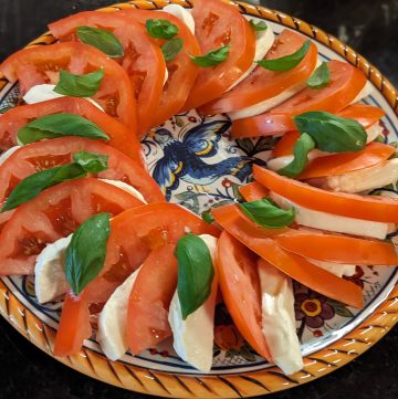 Caprese Salad with Tomato Slices, Fresh Mozzarella Slices and Basil Leaves arranged on a serving plate