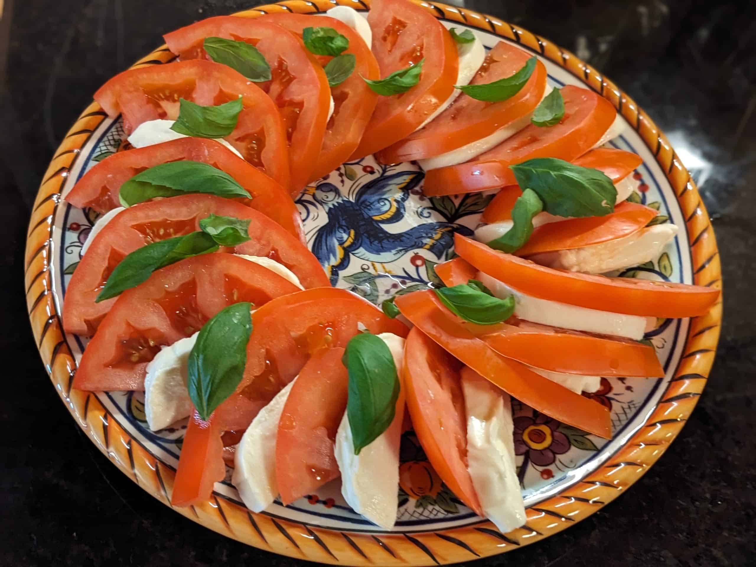 Caprese Salad with Tomato Slices, Fresh Mozzarella Slices and Basil Leaves arranged on a serving plate