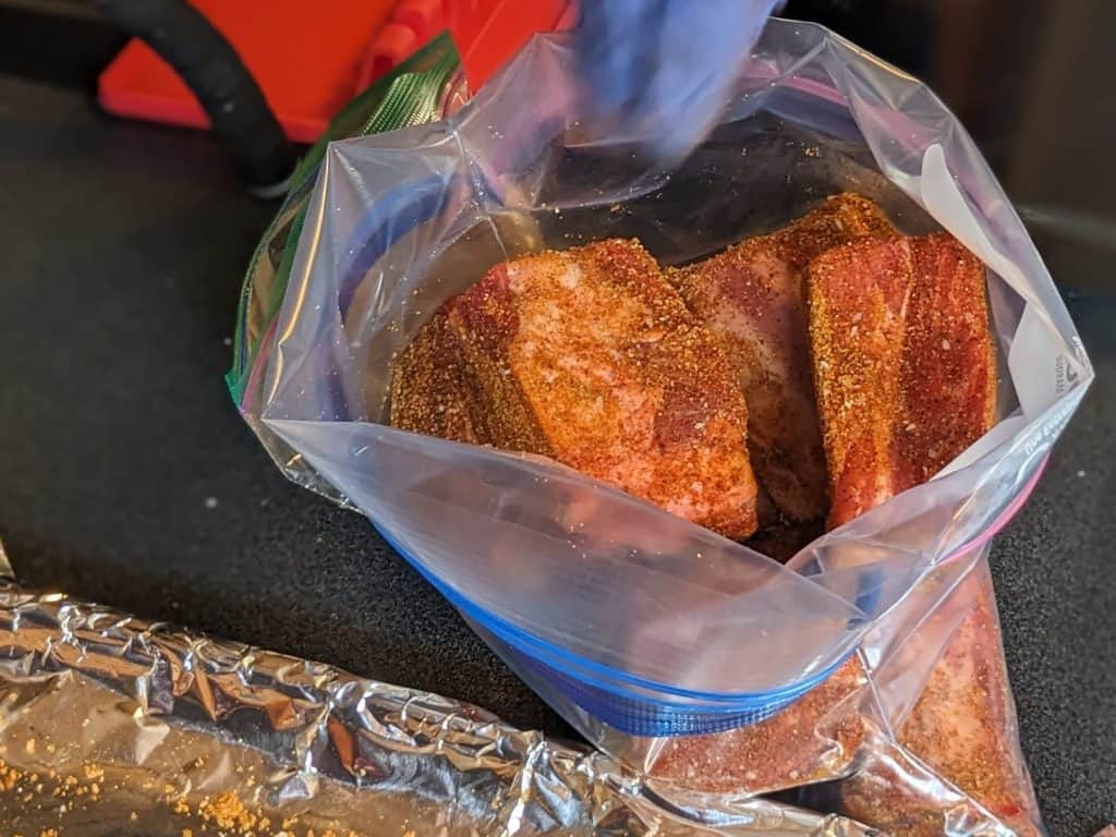 Placing seasoned raw beef short ribs in a plastic Ziploc bag