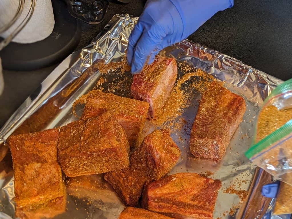 Rubbing a spice mix on raw beef short ribs on a foil-lined baking sheet
