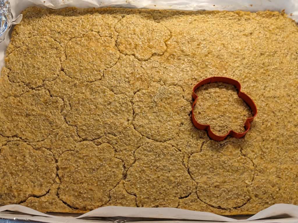 Cutting out cauliflower chia cakes with a paw print cookie cutter on a large rimmed baking sheet
