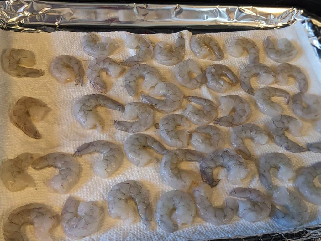 Raw shrimp laid out to dry on paper towel lined baking sheet