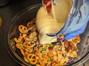 Pouring melted sugar free white chocolate onto snack mix