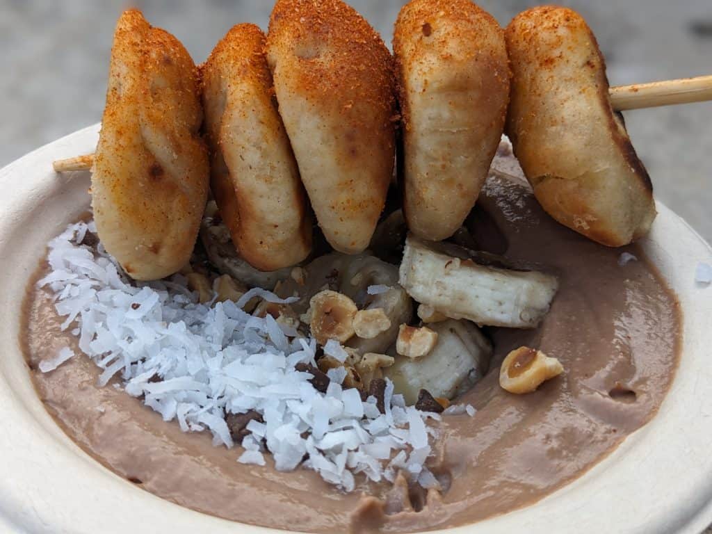 Choco-Nuts Hummus Bowl - bowl filled with chocolate hazelnut hummus topped with hazelnuts, coconut shreds, and sliced bananas, served with BBQ dry rub dusted pita puffs