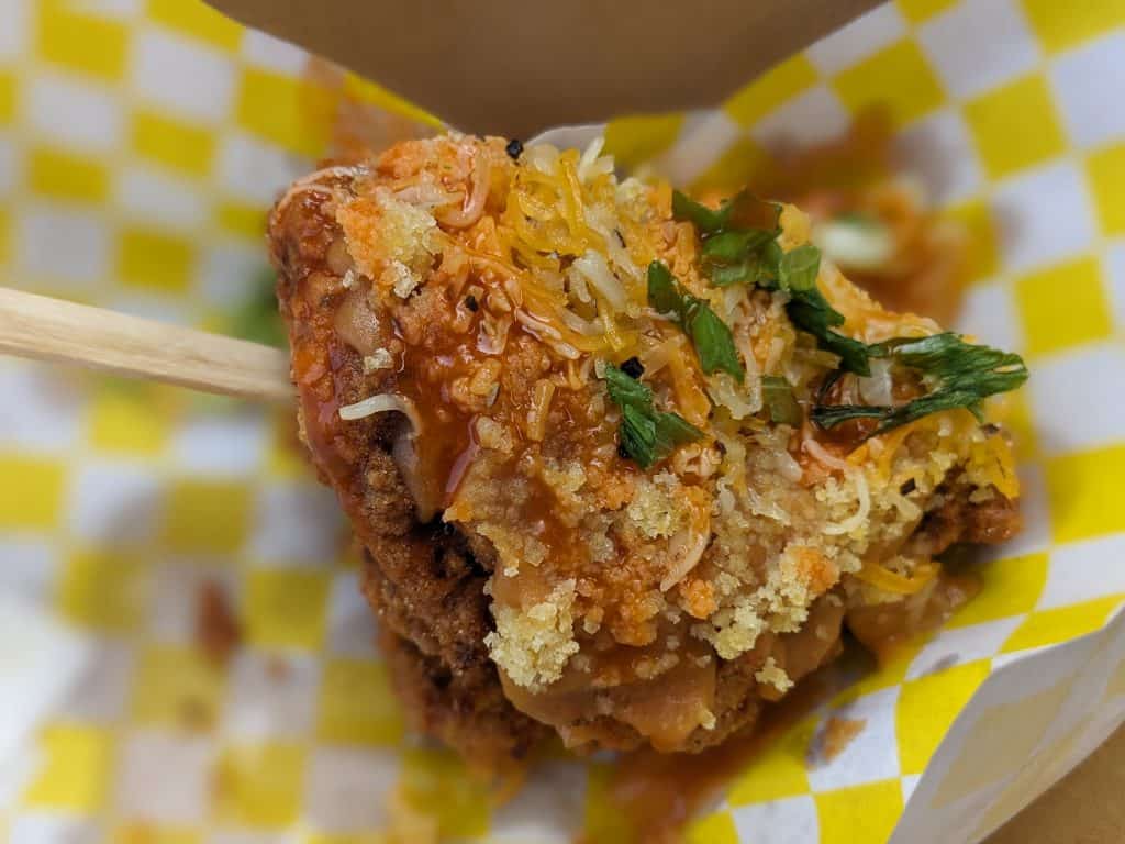 Soulsicle in a paper basket - fried chicken with cornbread crumbs, candied yam sauce, hot sauce, cheddar cheese, and green onions