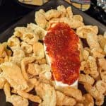 Brie cut in a coffin shape and covered with chili garlic sauce on a plate surrounded by pork rinds