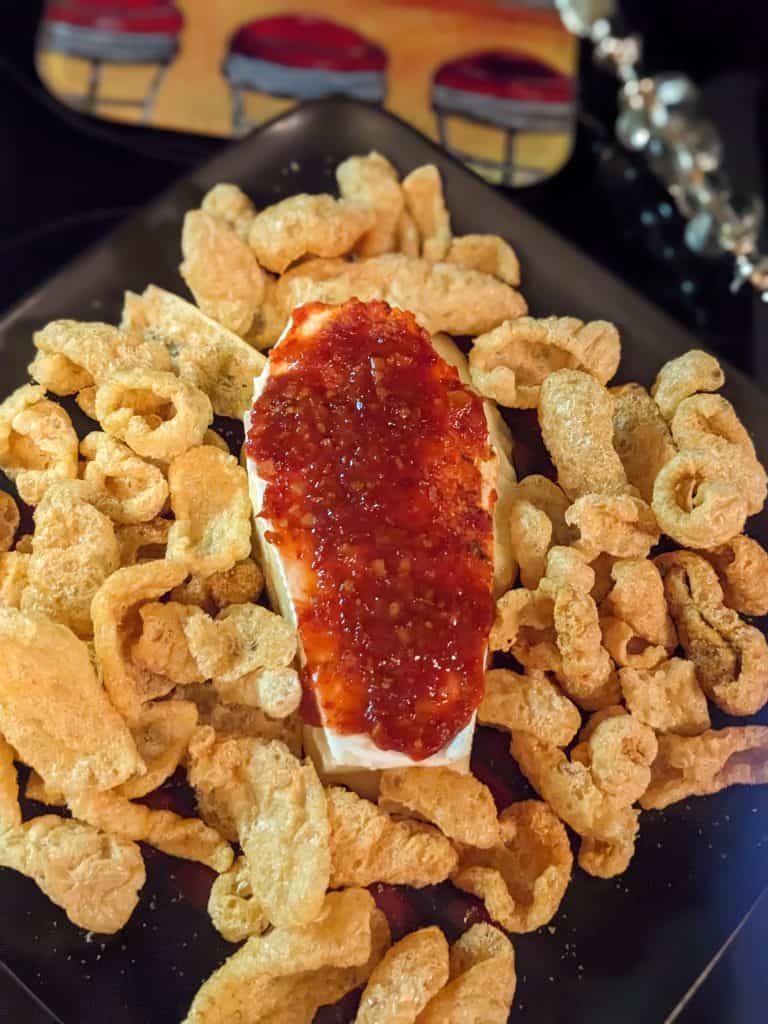 Brie cut in a coffin shape and covered with chili garlic sauce on a plate surrounded by pork rinds