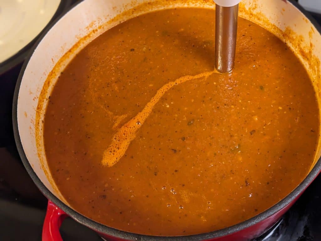 Roasted Tomato Poblano Soup in Dutch oven being blended with an immersion blender