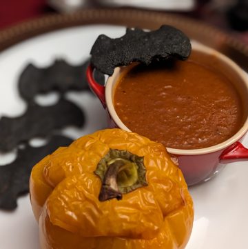 Plated bowl of Roasted Tomato Poblano Soup with Keto Black Bat Crackers and a Stuffed Pepper Jack-O-Lantern