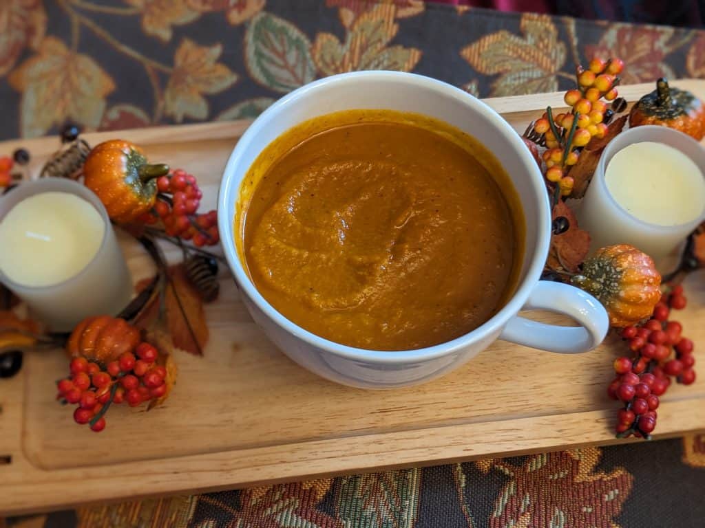 Savory Pumpkin Soup in a white cup / bowl between two fall candles on fall table runner