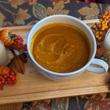 Savory Pumpkin Soup in a white cup / bowl between two fall candles on fall table runner
