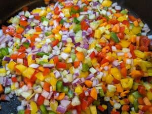 Diced vegetables being cooked in a pan for stuffing mix for Stuffed Peppers. Veggies include, red bell peppers, green bell peppers, yellow bell peppers, red onions, carrots, and celery.