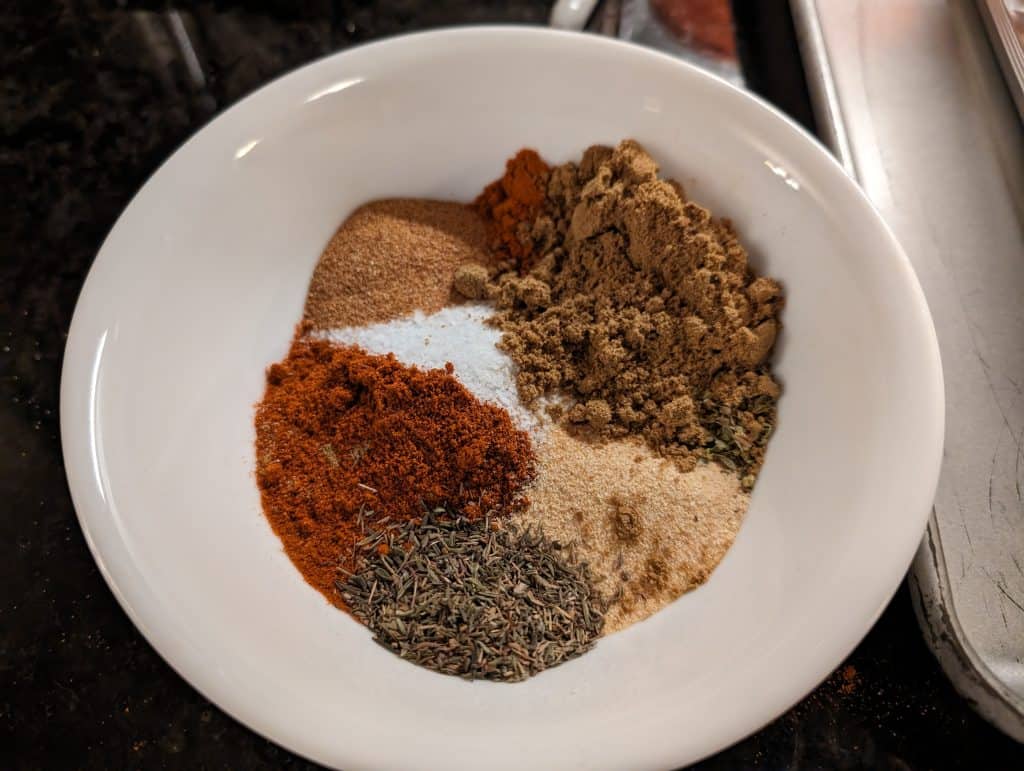 Bowl containing the mix of spices for Easy Keto Pot Roast, including: cumin, paprika, garlic powder, onion powder, kosher salt, oregano, thyme, cayenne, and ground black pepper