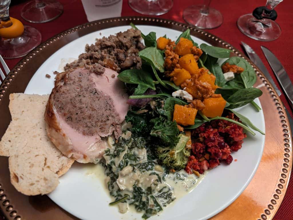 Holiday Party Dinner Plate containing: Turkey Roulade, slice of Cottage Loaf bread, Pepper Jack Creamed Spinach, Cranberry Pomegranate Relish, Winter Salad, Butternut Squash and Sausage Bake over Spinach, and Greek Stuffing