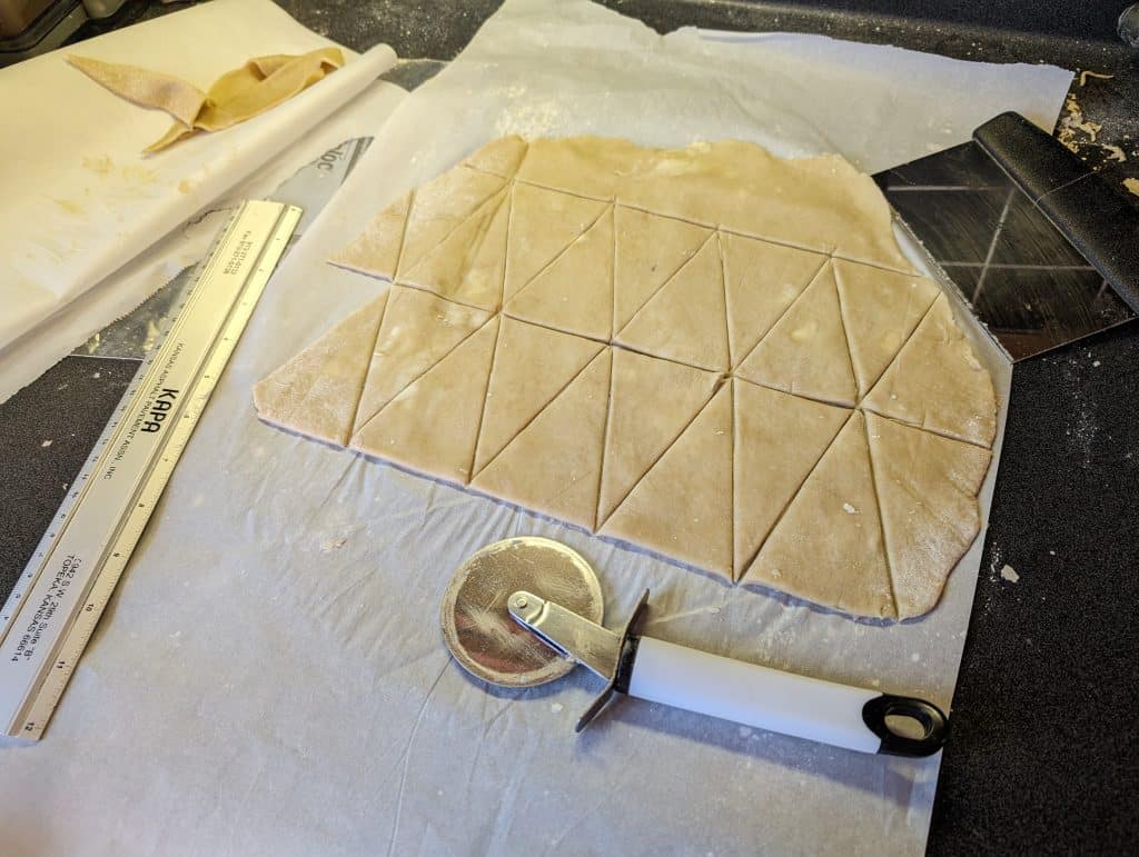 Keto Butter Horn Cookie Dough being measured and cut with a ruler, pizza cutter, and bench scraper