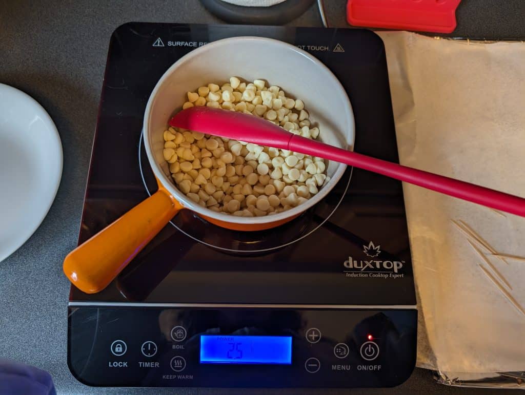 Sugar free white chocolate chips in a ceramic-coated cast iron pan on an induction burner ready to be melted