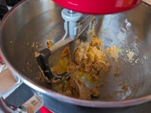 Adding eggs to dough mixture for Keto Peanut Butter Cookie Cups in the bowl of a stand mixer