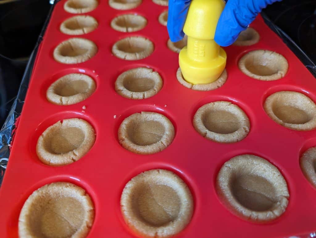 Using a tart mold to press indentations into cookie cups in a silicone mini muffin pan