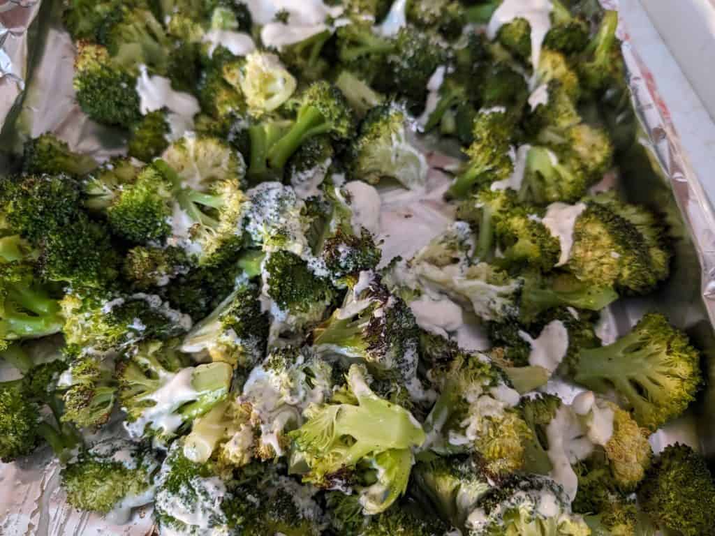 Roasted broccoli on a rimmed baking sheet being dressed with Caesar dressing
