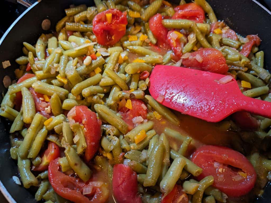 Cooking green beans with stewed tomatoes, onions, and peppers in a pan