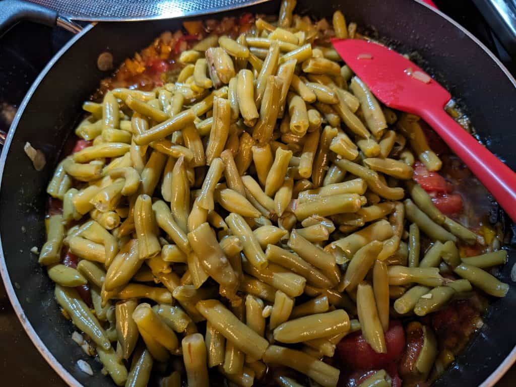 Cooking green beans in a pan with stewed peppers and onions