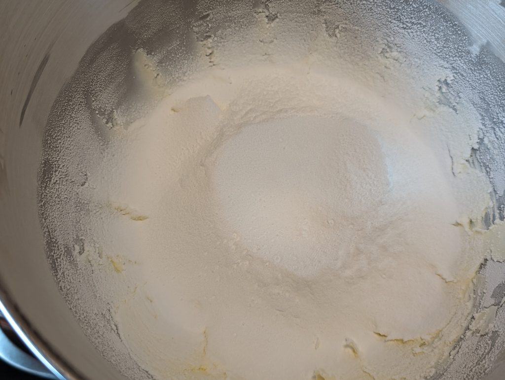 Powdered sweeteners in mixing bowl with beaten cream cheese and butter