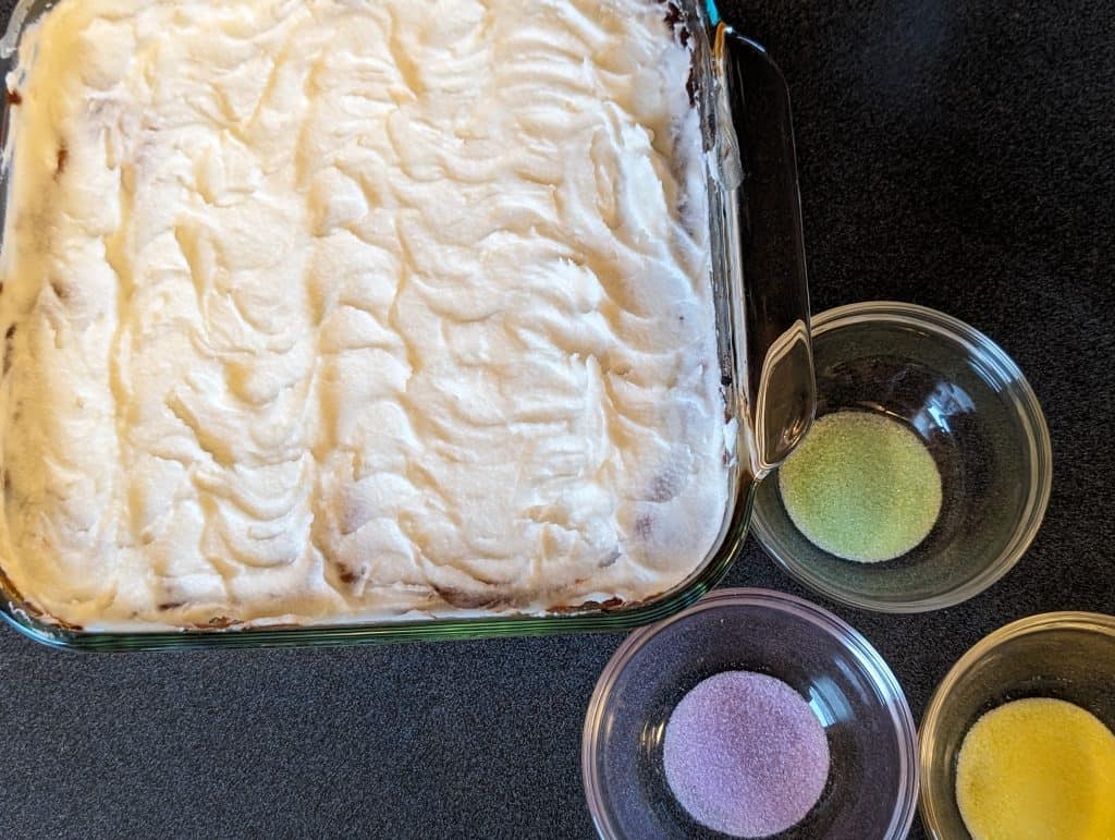 Frosted King Cake Earthquake Cake next to three colors of granulated erythritol for decoration--green, purple, and yellow