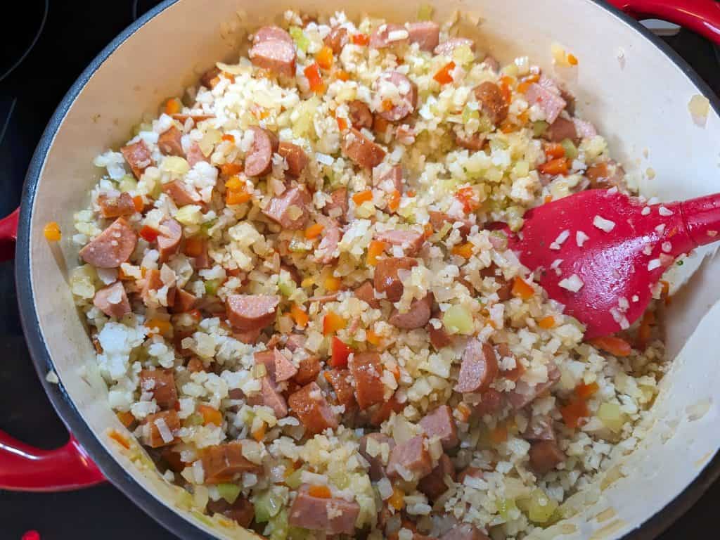 Adding cauliflower rice and diced tomatoes to a pot of Low Carb Jambalaya