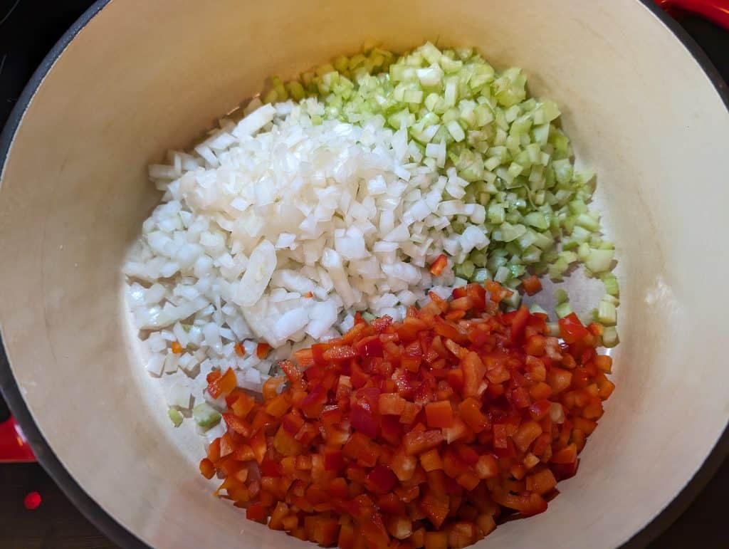 Diced onions, celery, and bell peppers in a Dutch Oven ready to be sautéed