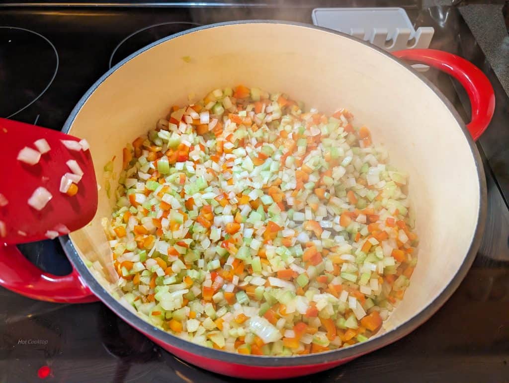 Softened, diced onions, celery, and bell peppers cooking in a Dutch oven