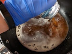 Pouring beer into a pan for braising sausages.