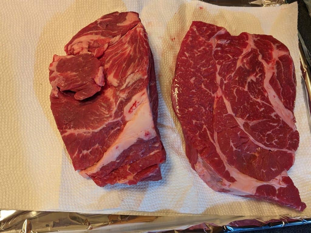 2 beef chuck roasts being patted dry on a paper towel lined baking sheet