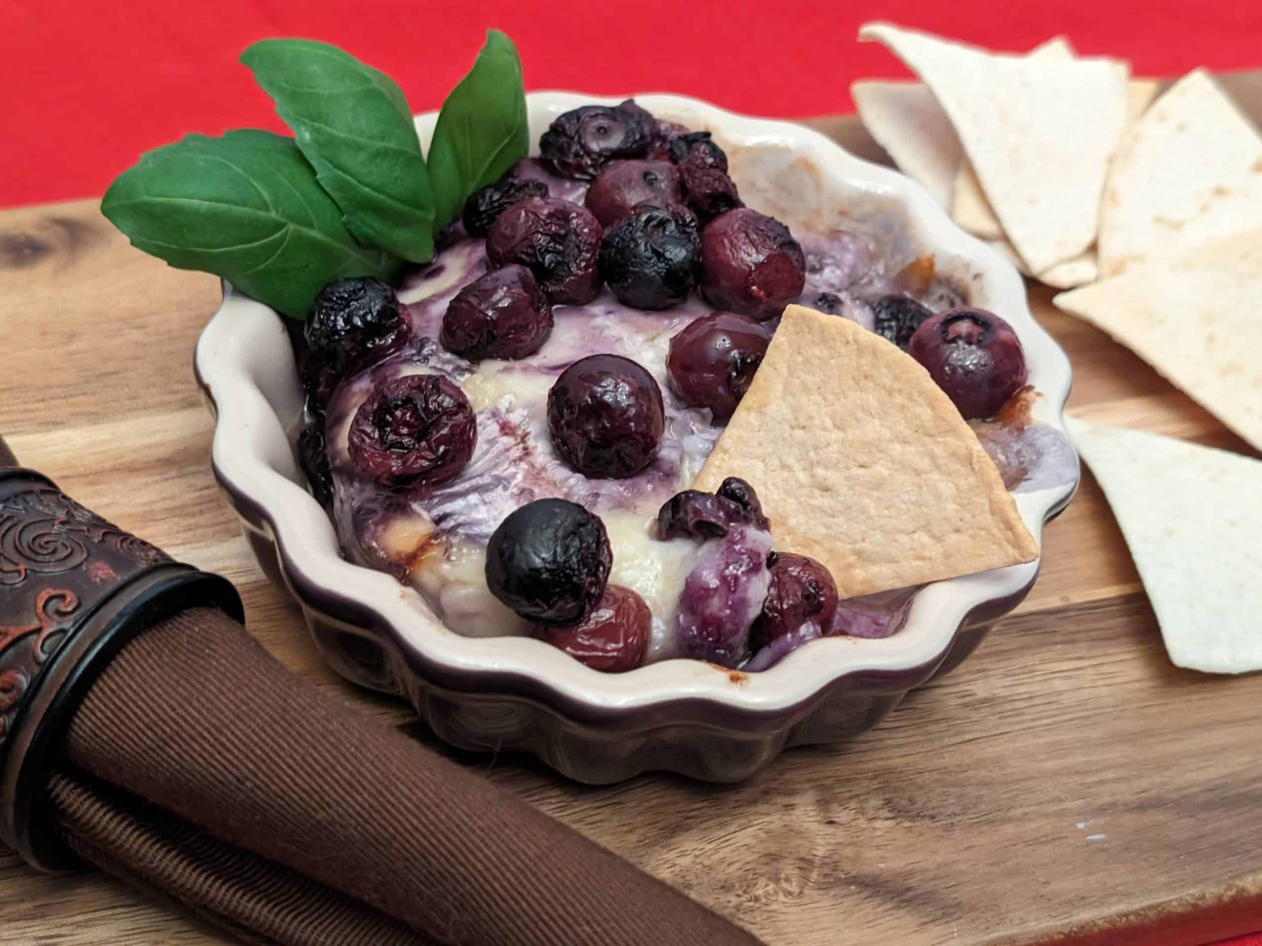 Baked Brie and Keto Pickled Blueberries in a dish with a keto chip and some basil leaves for decoration