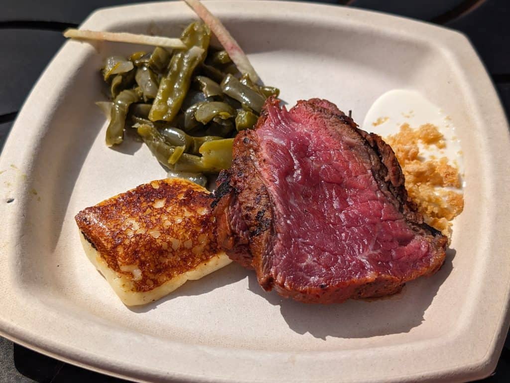 Two slices of carne asada on a plate with fried cheese, pickled peppers and a Oaxaca cheese foam