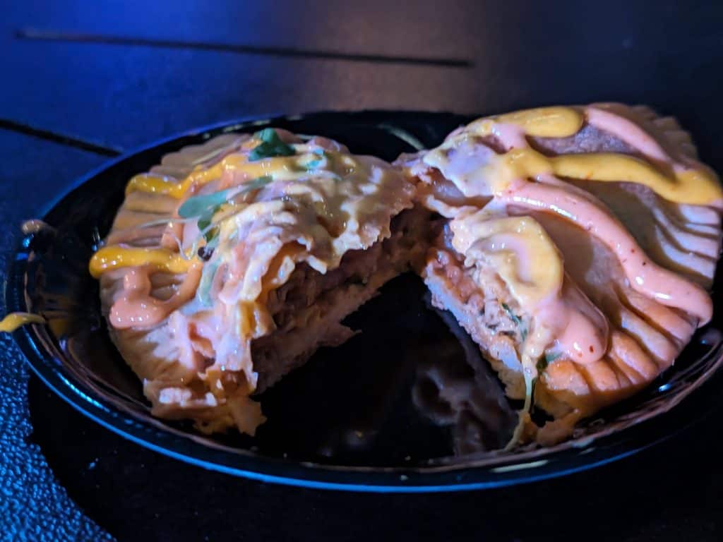 A Chorizo and Potato Empanada drizzled with two spicy mayo sauces cut open for a cross-section view