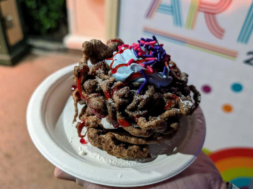 Ice cream sandwich made with chocolate funnel cakes and drizzled with raspberry sauce and topped with whipped cream and sprinkles