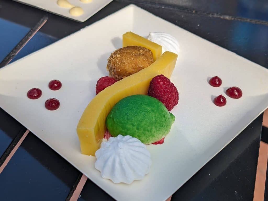 A Deconstructed Key Lime Pie consisting of meringues, a lime custard shaped and colored like a lime, fresh raspberries, gelatinized lime curd, a mini cake, and dollops of raspberry coulis