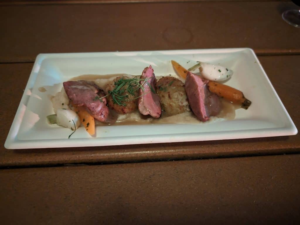 Slices of duck breast and ricotta dumplings on a plate with roasted mini carrots and turnips with a gravy