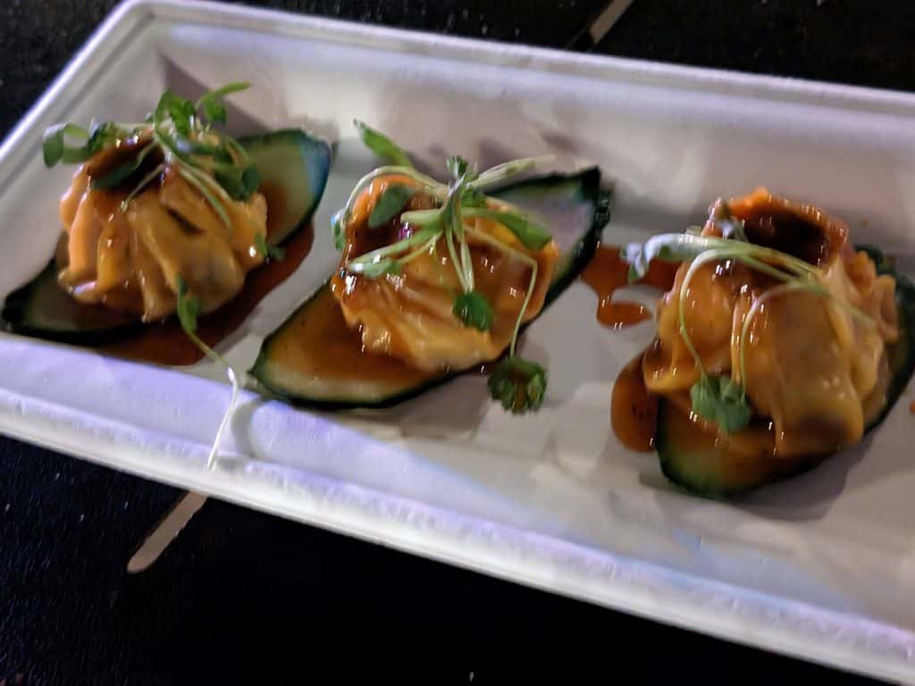 Plate with 3 General Tso's Chicken Shumai plated on slices of cucumber with dark, sweet sauce