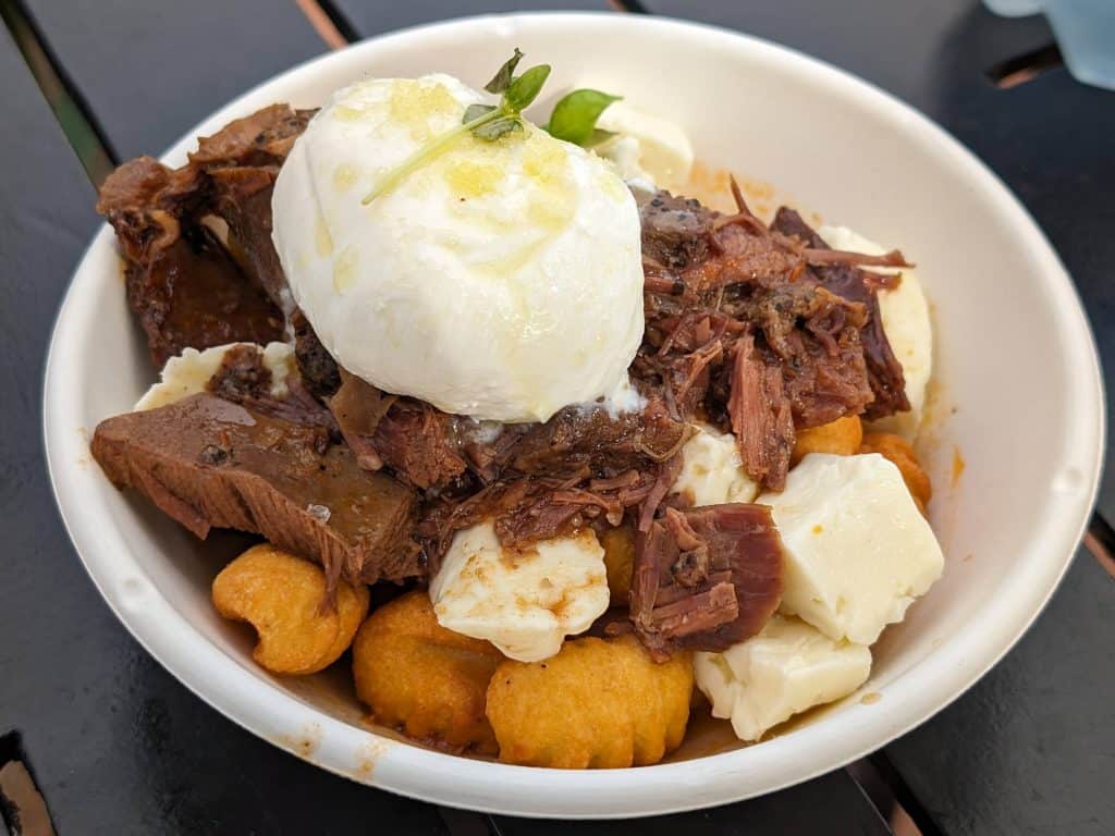 A bowl of Gnocchi Poutine with fried gnocchi, cheese curds, braised beef, and burrata