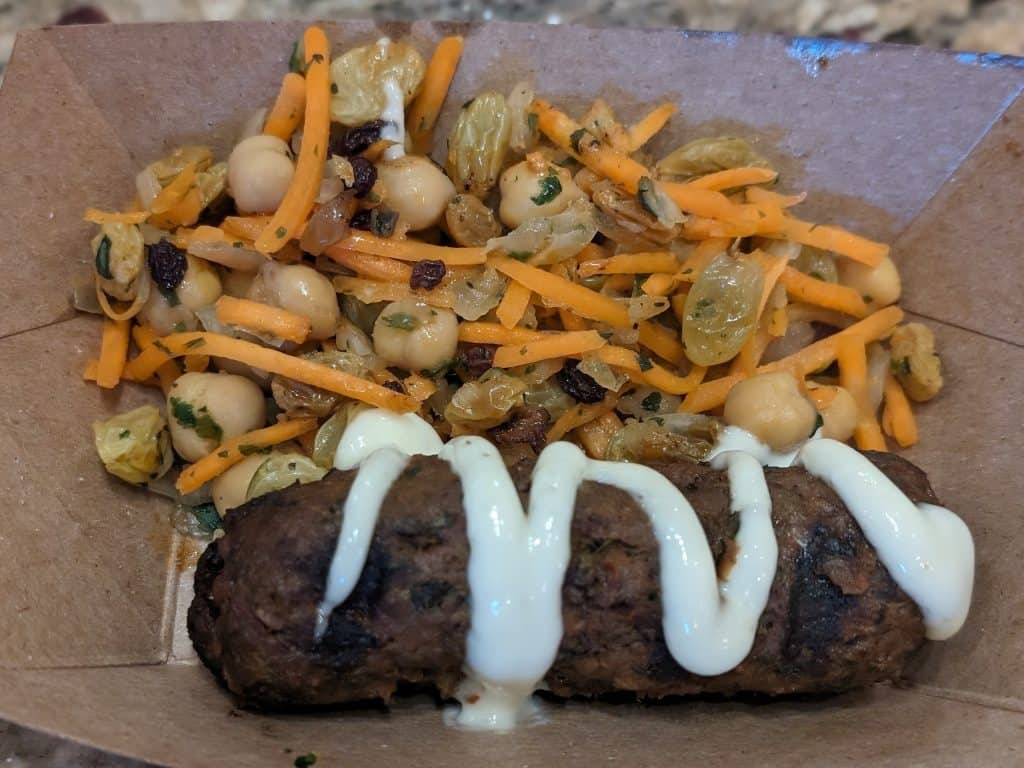 Spiced lamb kebab drizzled with garlic aioli in a tray with a carrot-chickpea salad