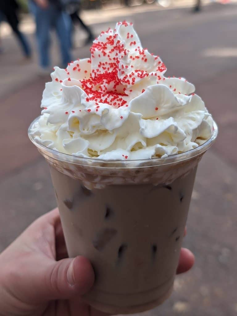 Realism Roseberry Cold Brew topped with whipped cream and red sprinkles in a plastic cup