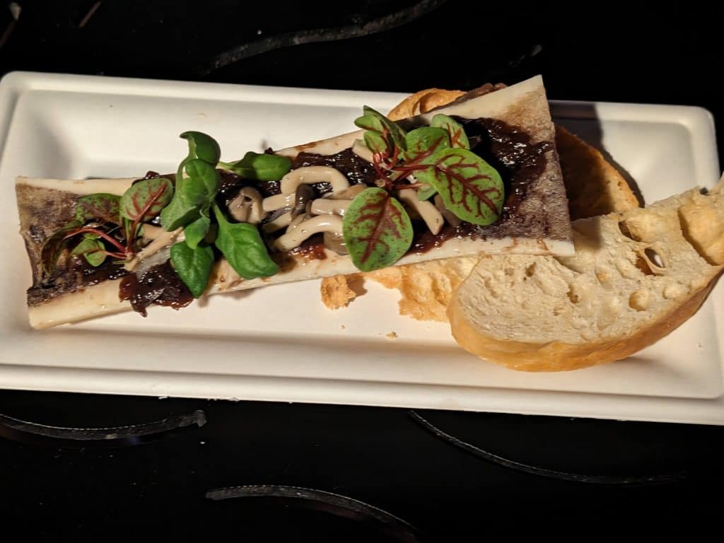 Bone containing Roasted Bone Marrow with Onion Marmalade, Pickled Mushrooms and Petite Lettuce on a plate with toasted sourdough bread