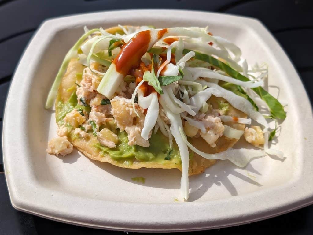 A crispy street taco tortilla covered with guacamole, chilled fried lobster, and a pickled slaw with hot sauce