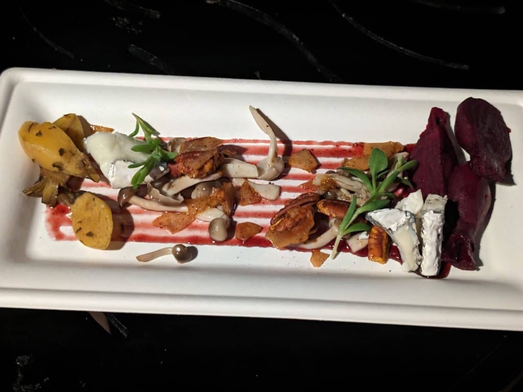 An artfully arranged plate of roasted golden and purple beets with goat cheese, mushrooms, petite lettuce, blackberry gastrique, and spiced pecans